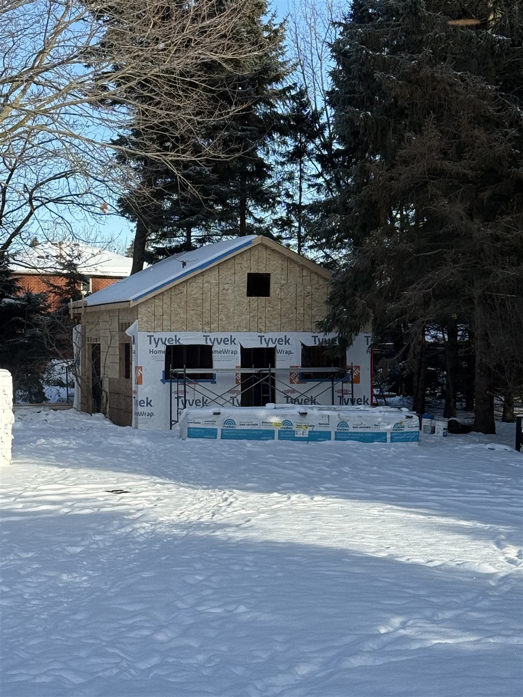 The workshop during construction in winter, with sheathed walls, house wrap and scaffolding across the front